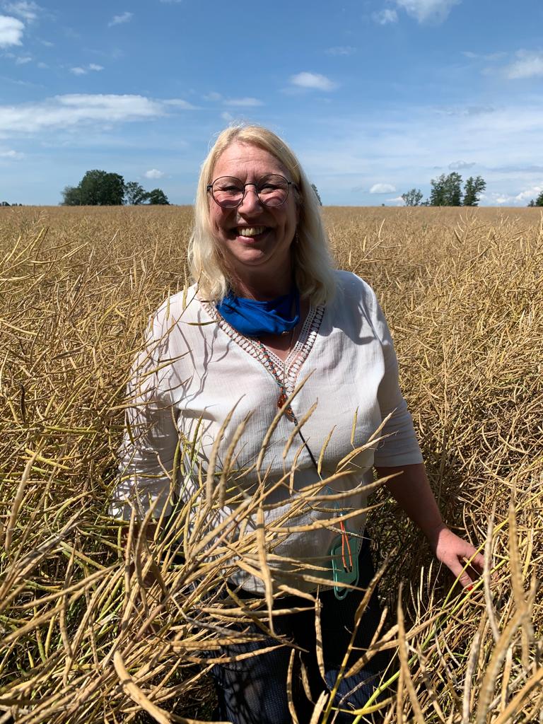 Gabi Brill steht lächelnd in einem blühenden Rapsfeld